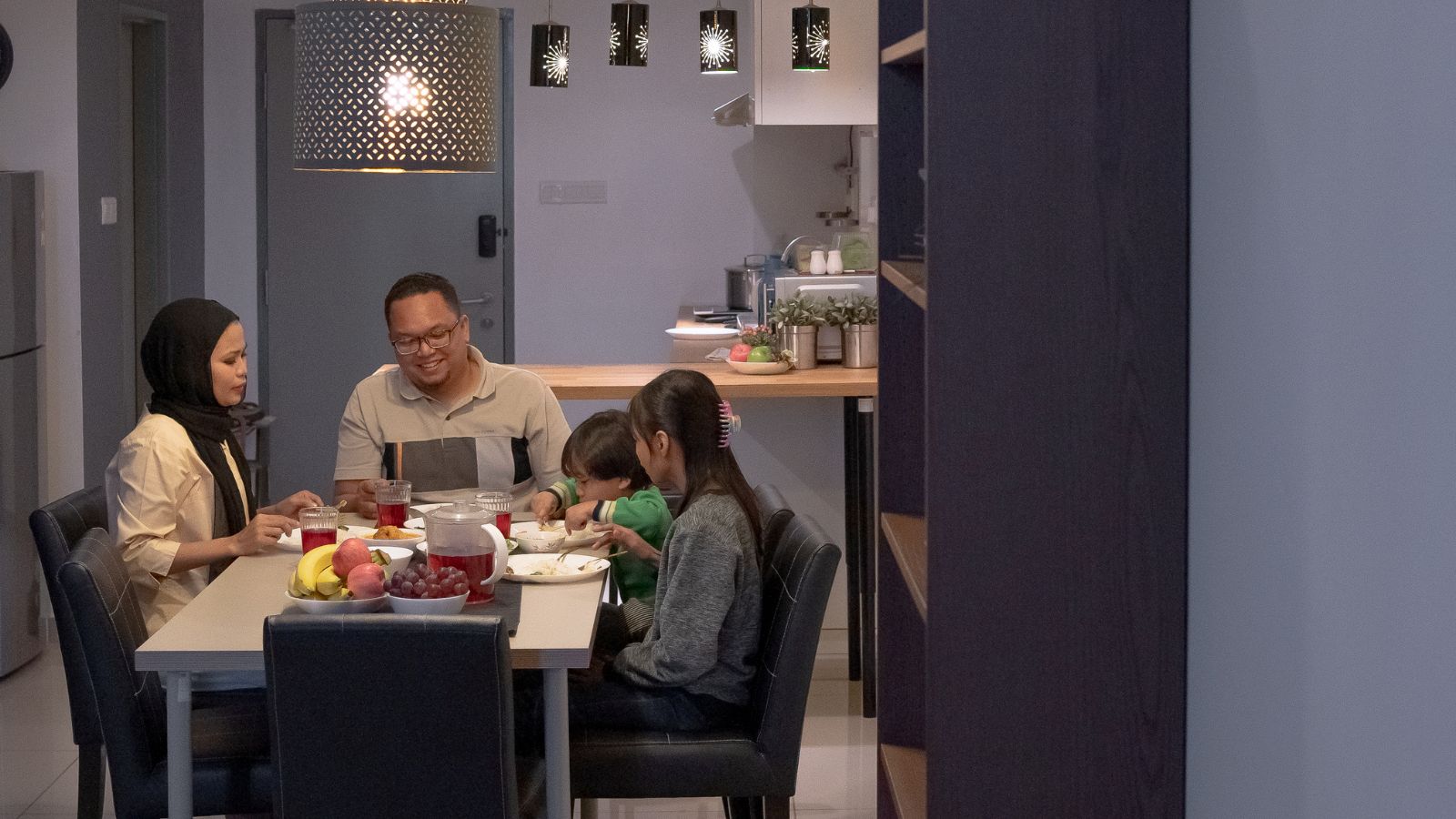 Une famille dîne autour de la table le soir, dans une cuisine éclairée par une suspension.