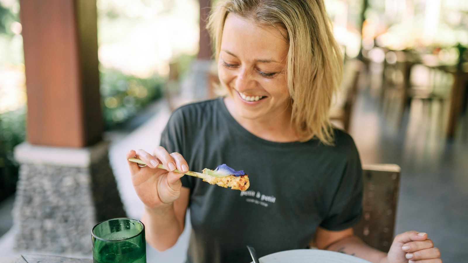 Attablée en terrasse, une femme déjeune calmement, une brochette à la main.
